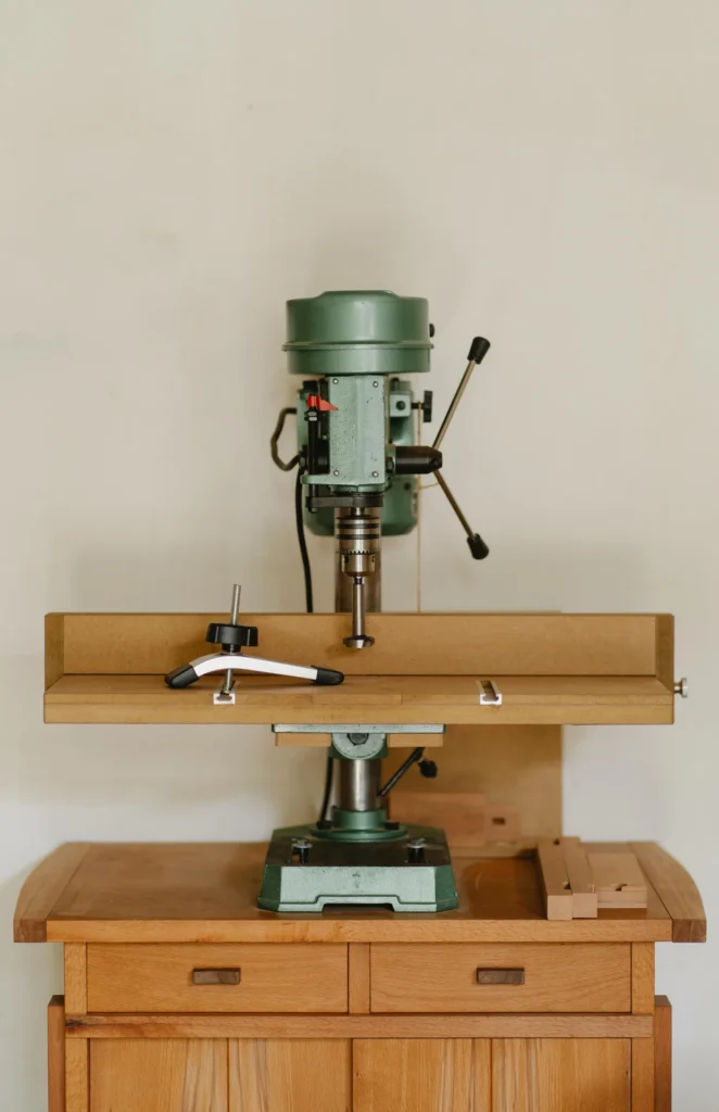 massivholz-kommode-tischbohrmaschine.webp Kommode aus hellem Massivholz mit Schubladen und Türen, darauf eine Tischbohrmaschine