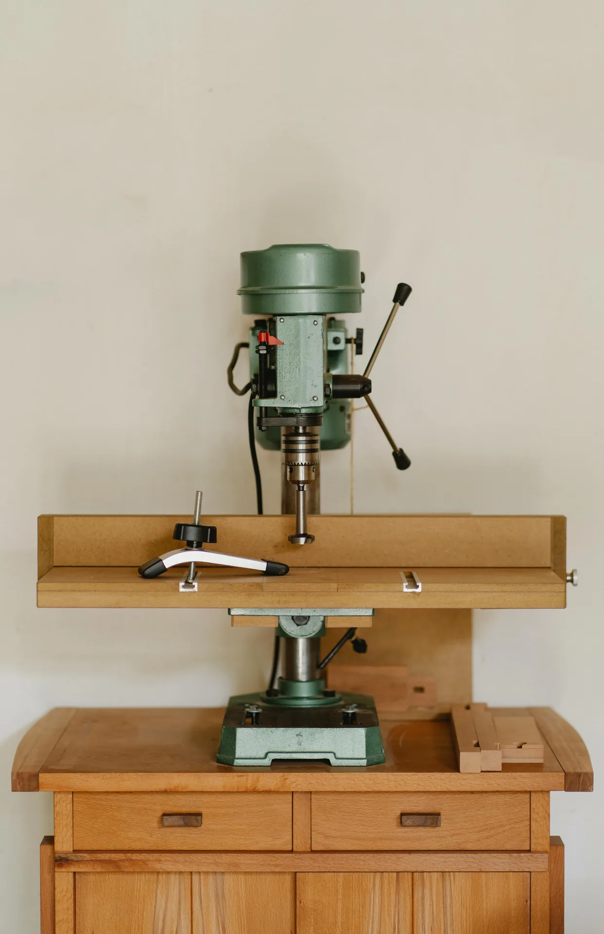 massivholz-kommode-tischbohrmaschine.webp Kommode aus hellem Massivholz mit Schubladen und Türen, darauf eine Tischbohrmaschine
